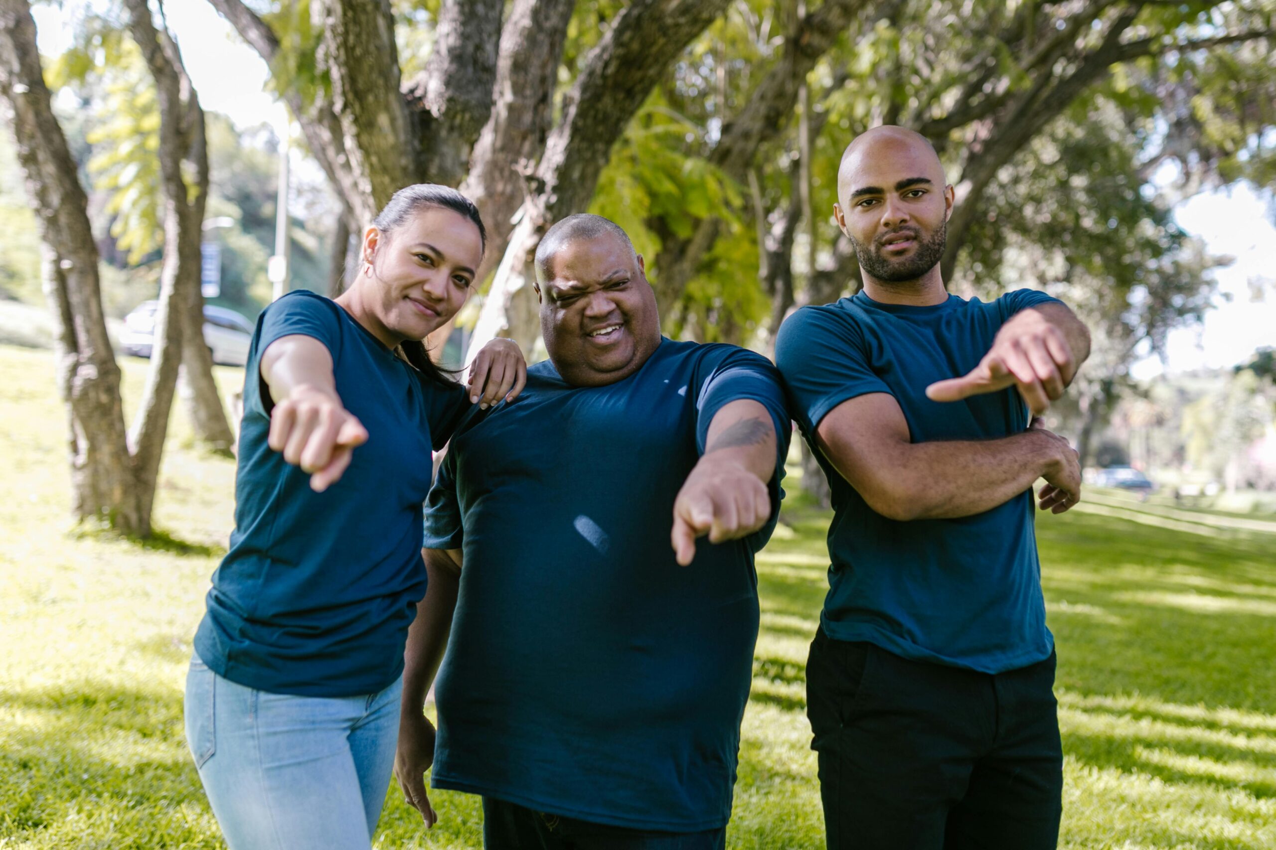 Three adults pointing at the camera during an outdoor team building activity in a park.